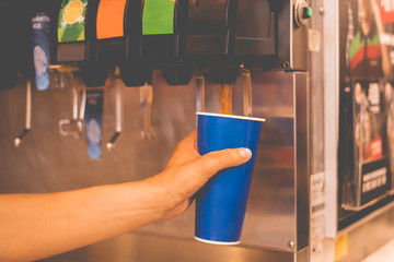 Wall Mural - hand holding a paper glass to pour the lemonade soda soft drink  machine  in a fastfood restaurant