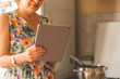 © Mihail - housewife woman holding a gadget smartphone or tablet to check receipt while cooking at the kitchen