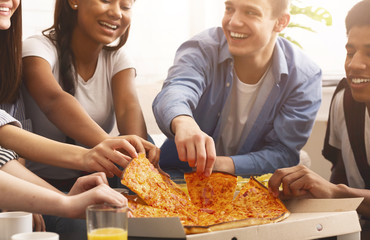 Teen friends taking slices of hot pizza from cardboard box