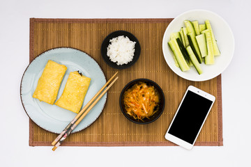 Wall Mural - Fried spring rolls; salad; boiled rice and sliced zucchini with cell phone over placemat