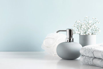 Soft light bathroom decor in pastel blue color, towel, soap dispenser, white flowers, accessories on white wood shelf. Elegant decor bathroom interior.