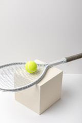 Wall Mural - bright yellow tennis ball with racket on cube on white background