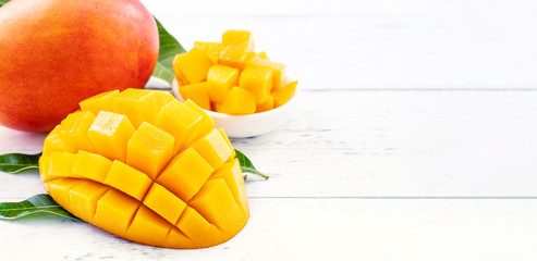 Beautiful chopped mango chunks with green leaves on bright white color timber background. Copy space, close up, macro. Tropical fruit concept.