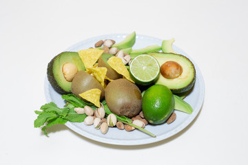 Plate with salad made of healthy food for diet – Fresh organic green meal – Vegetable mix of avocado, almonds, pistachios, kiwi, lime and some tortillas pieces