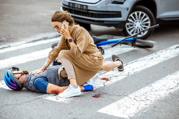 Wall Mural - Road accident with injured cyclist lying on the pedestrian crossing near the broken bicycle, worried woman driver calling and checking men's pulse