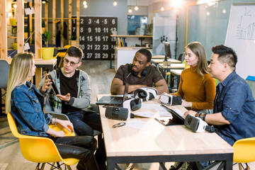 Teamwork trying devices and virtual reality glasses for work in creative office. Five diverse young people using new technology at startup. Trends , social and business concept