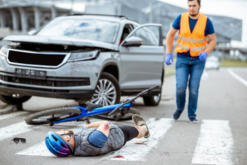 Wall Mural - Road accident with injured cyclist lying on the pedestrian crossing near the broken bicycle and car driver running on the background