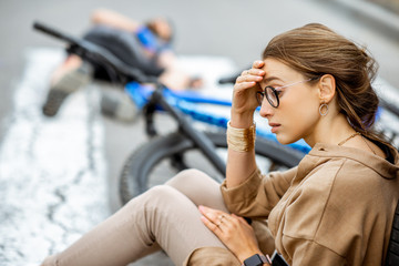 Wall Mural - Sad woman sitting near the car, worried of injured man lying on the pedestrian crossing after the road accident