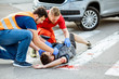 Medic with car driver applying first aid to the injured man lying on the pedestrian crossing after the road accident