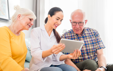 Nurse showing medical raport using tablet to senior couple at home