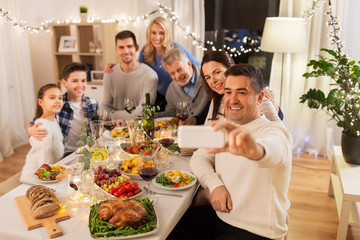 Wall Mural - celebration, holidays and people concept - happy family having dinner party at home and taking selfie by smartphone