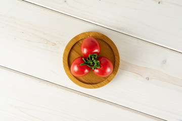 Group of three whole fresh red tomato cherry on a bamboo plate flatlay on white wood