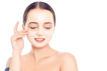 Wall Mural - Brunette in a white mask for the face. Beautiful photo of a girl with perfect skin. A young girl cares for herself. Studio photo on a white background.