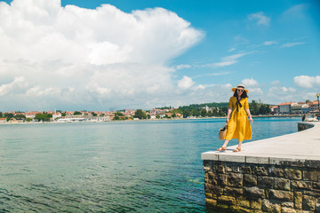 Wall Mural - woman standing on the stone edge pier looking at sea. yellow sundress