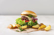© Natasha Breen - Homemade fast food burger classic hamburger or cheeseburger with beef, salad, cheese and tomato served on paper with baked country potatoes on white marble kitchen table. Copy space.