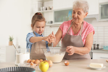 Canvas Print - Cute girl and her grandmother cooking in kitchen