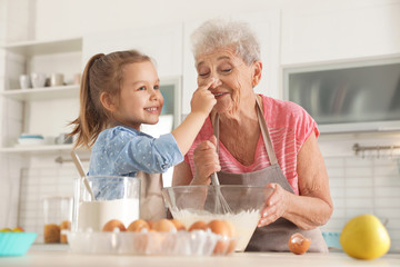 Canvas Print - Cute girl and her grandmother cooking in kitchen