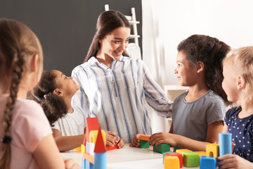 Poster - Cute little children and nursery teacher playing with building blocks in kindergarten. Indoor activity