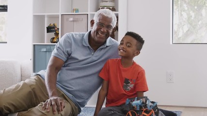 Wall Mural - Portrait Of Grandfather With Grandson Sitting On Rug At Home Building Model Helicopter Together