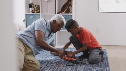 Wall Mural - Grandfather With Grandson Sitting On Rug At Home Building Model Helicopter Together