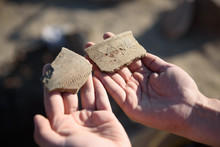 An Archaeologist At An Archaeological Site Shows Fragments Of Ancient Pottery In The Hands Of