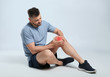 © New Africa - Full length portrait of man with knee problems sitting on grey background