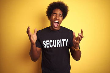 Sticker - American safeguard man with afro hair wearing security uniform over isolated yellow background celebrating mad and crazy for success with arms raised and closed eyes screaming excited. Winner concept