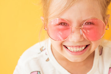 Smiling little girl in big round pink glasses on yellow background