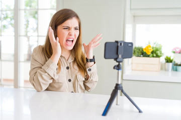 Poster - Beautiful young woman doing online video call using smartphone webcam crazy and mad shouting and yelling with aggressive expression and arms raised. Frustration concept.