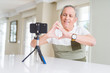 © Krakenimages.com - Handsome senior man doing video conference talking to the smartphone camera smiling in love showing heart symbol and shape with hands. Romantic concept.