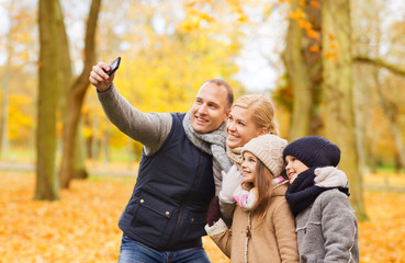 Wall Mural - family, childhood, season, technology and people concept - happy family taking selfie with smartphone in autumn park