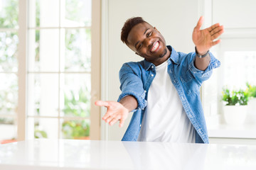 Sticker - Handsome african american man at home looking at the camera smiling with open arms for hug. Cheerful expression embracing happiness.