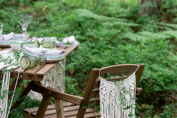 Boho style wedding reception dinning table with macrame tablecloth, decoration on a rustic wooden table