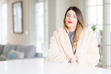 Sticker - Young beautiful woman wearing winter fur coat at home with serious expression on face. Simple and natural looking at the camera.