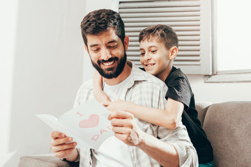 Happy father's day! Son congratulating dad and giving him a greeting card. Daddy and son smiling and hugging. Family holiday and togetherness.