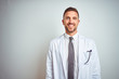 © Krakenimages.com - Young handsome doctor man wearing white profressional coat over isolated background with a happy and cool smile on face. Lucky person.