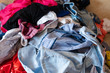 © Вячеслав Косько - Front view of colorful childish clothes scattered on sofa at home. Big bunch of clothes lying at room before laundry. Concept of cleaning, mess, mud and household chores.