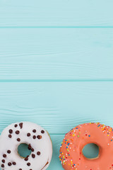 Two different donuts on blue wooden background. Pastry decorated with colorful icing. Holiday of taste.