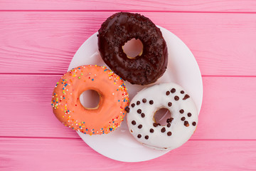 Three donuts on plate, top view. Different donuts on pink wooden background.