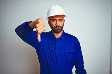 Sticker - Handsome indian worker man wearing uniform and helmet over isolated white background looking unhappy and angry showing rejection and negative with thumbs down gesture. Bad expression.