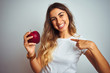 © Krakenimages.com - Young beautiful woman eating red apple over grey isolated background with surprise face pointing finger to himself