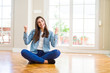 © Krakenimages.com - Beautiful young woman sitting on the floor at home celebrating surprised and amazed for success with arms raised and open eyes. Winner concept.