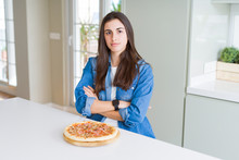 Beautiful Young Woman Eating Homemade Tasty Pizza At The Kitchen Skeptic And Nervous, Disapproving Expression On Face With Crossed Arms. Negative Person.