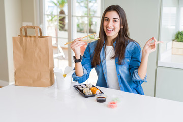 Sticker - Beautiful young woman eating asian sushi from home delivery very happy pointing with hand and finger to the side