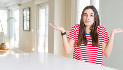 Poster - Beautiful young woman wearing casual stripes t-shirt clueless and confused expression with arms and hands raised. Doubt concept.