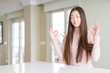 © Krakenimages.com - Beautiful Asian woman wearing casual sweater on white table relax and smiling with eyes closed doing meditation gesture with fingers. Yoga concept.