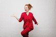 Slim positive caucasian girl in trendy red night-wear dancing on bricked background. Indoor photo of beautiful white young woman wears pajamas having fun at home.