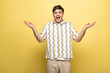 © LIGHTFIELD STUDIOS - cheerful young man showing shrug gesture and smiling at camera on yellow background