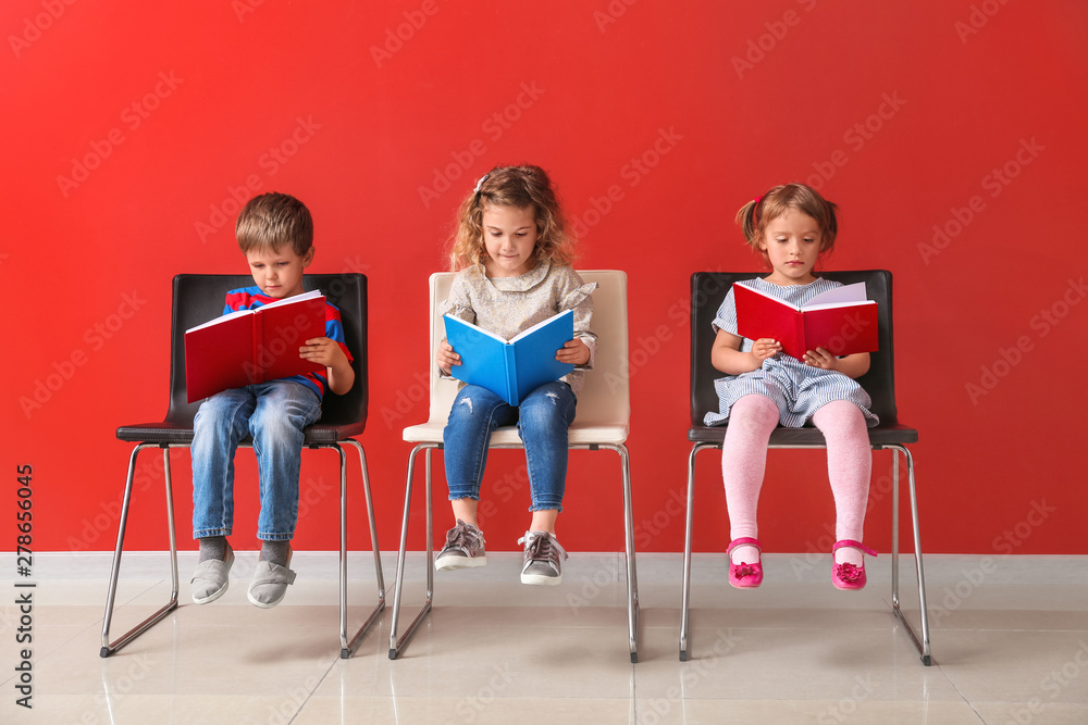 Cute little children reading books near color wall