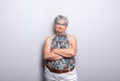 © FurryFritz - Elderly Woman with short gray hair and glasses posing in front of light gray wall with arms crossed wearing a self made neckholder top. the mature woman is looking at camera